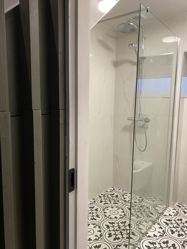 Una ducha con cerramiento de vidrio, pared de mármol blanco y baldosas de piso estampadas.