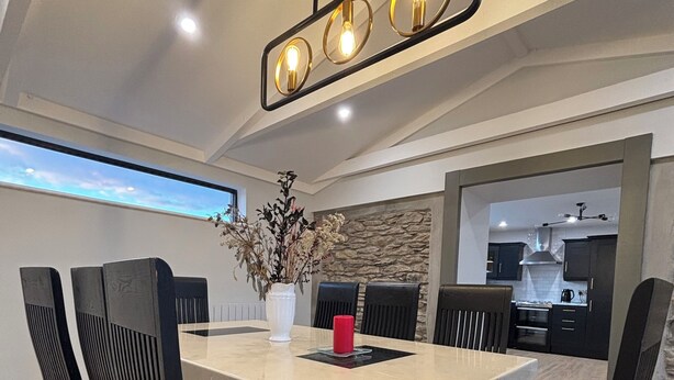 Un comedor moderno con una mesa rectangular, sillas acolchadas, un jarrón con flores secas y una lámpara colgante.