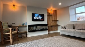 Una sala de estar moderna con chimenea, un televisor de pantalla plana montado en la pared, una silla de madera, un sofá y un tapete estampado.