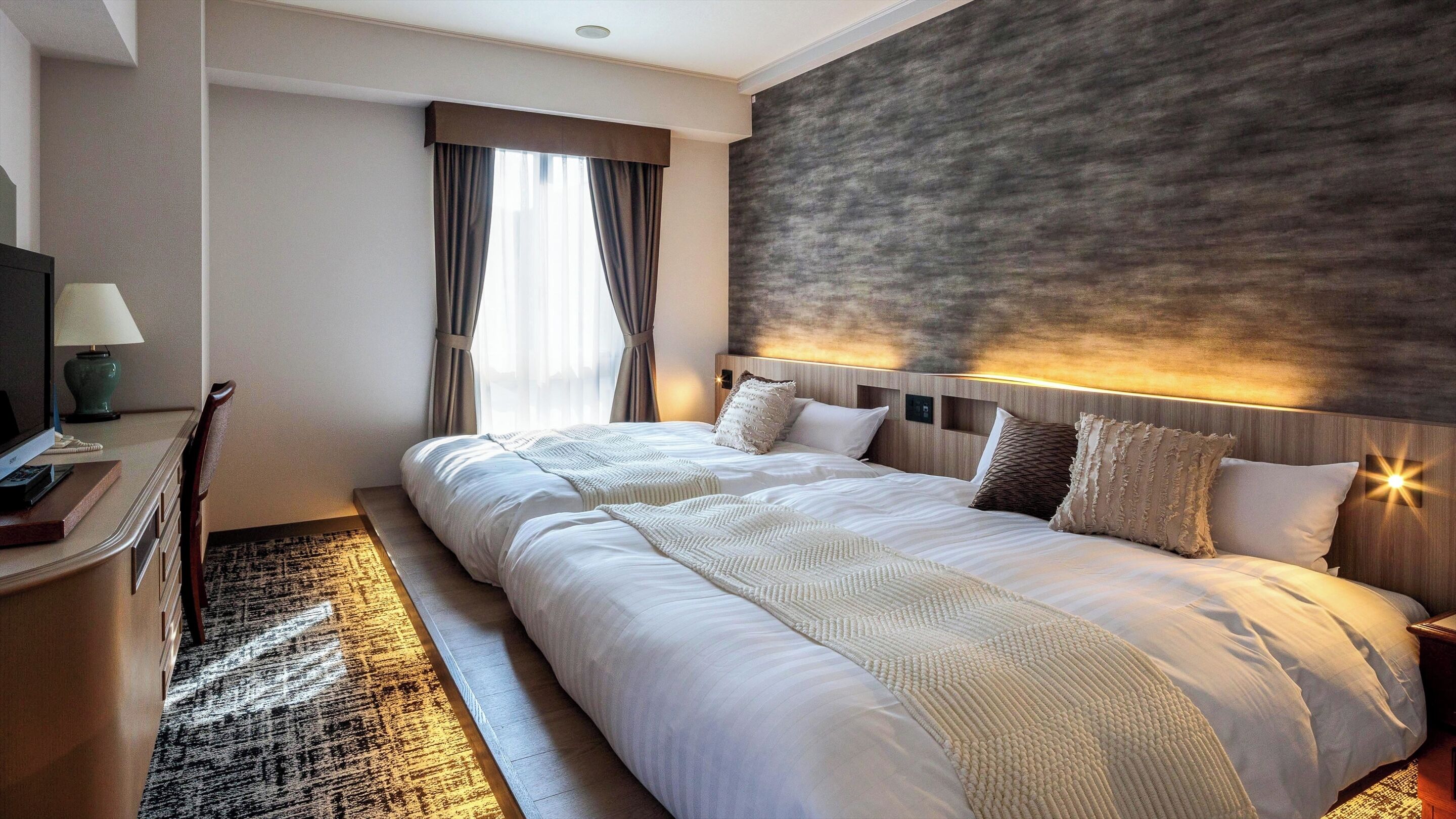 Una habitació d'hotel amb un llit gran, un escriptori amb una làmpada i una televisió.