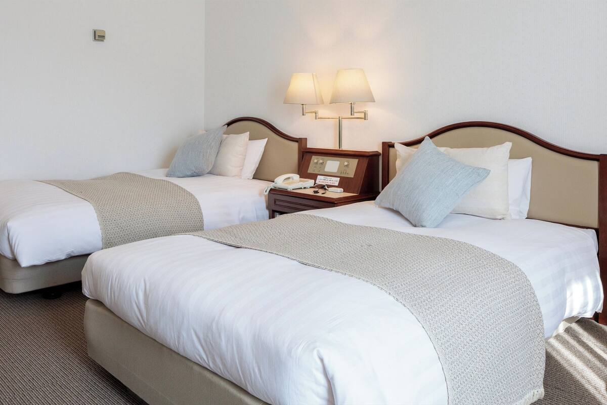 A hotel room with two beds, a bedside table with a lamp, and a telephone.