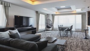 A modern hotel room with a flat-screen TV, a sofa, a hanging chair, a dining table with chairs, and a patterned carpet. - Gran Palette Hakodate (Hakodate)