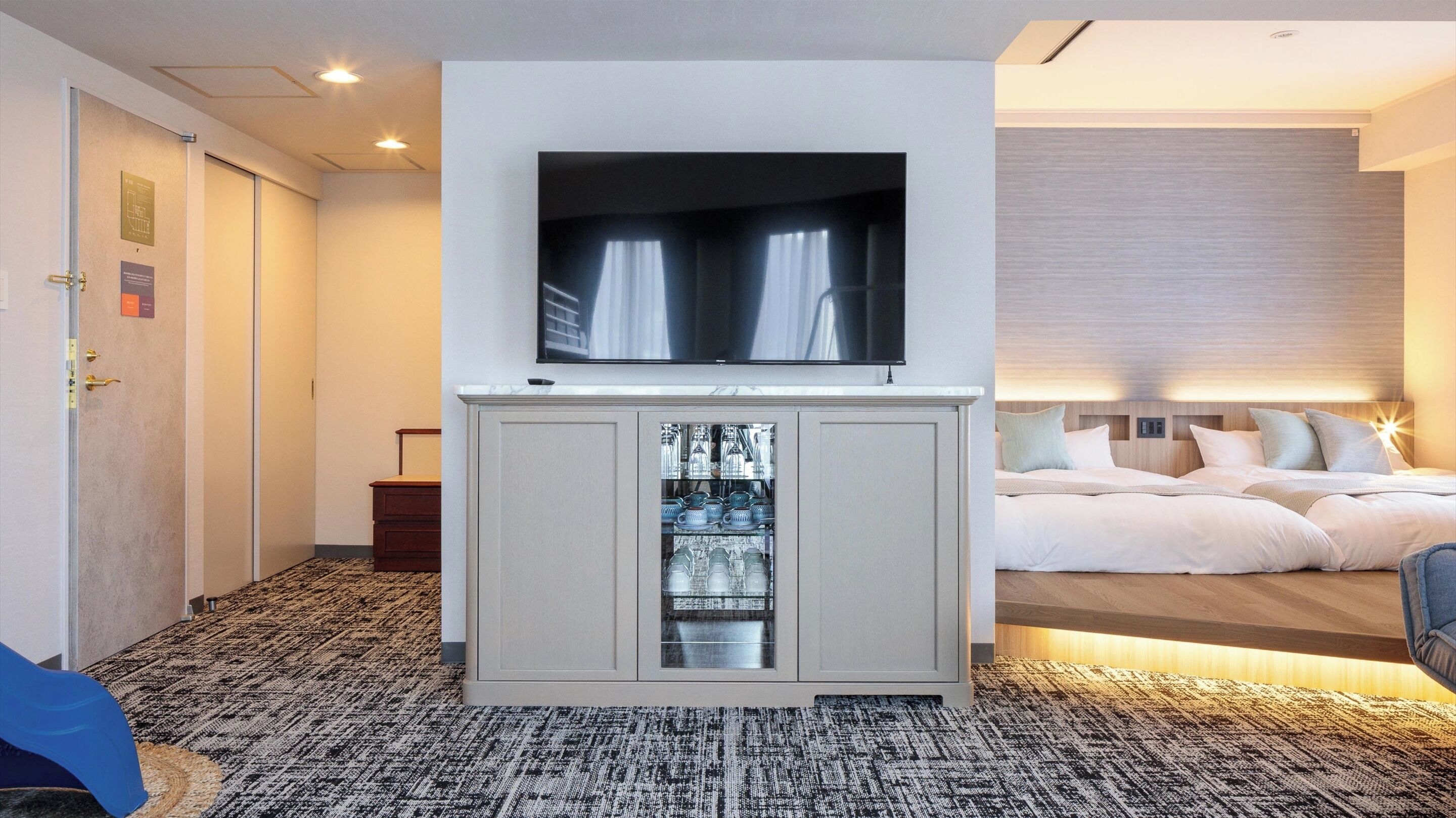 A hotel room with a TV mounted above a cabinet, a bed with a headboard, and a carpeted floor.