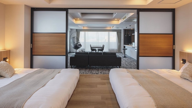 A hotel room with two beds, a dining area, and a view of the city. - Gran Palette Hakodate (Hakodate)