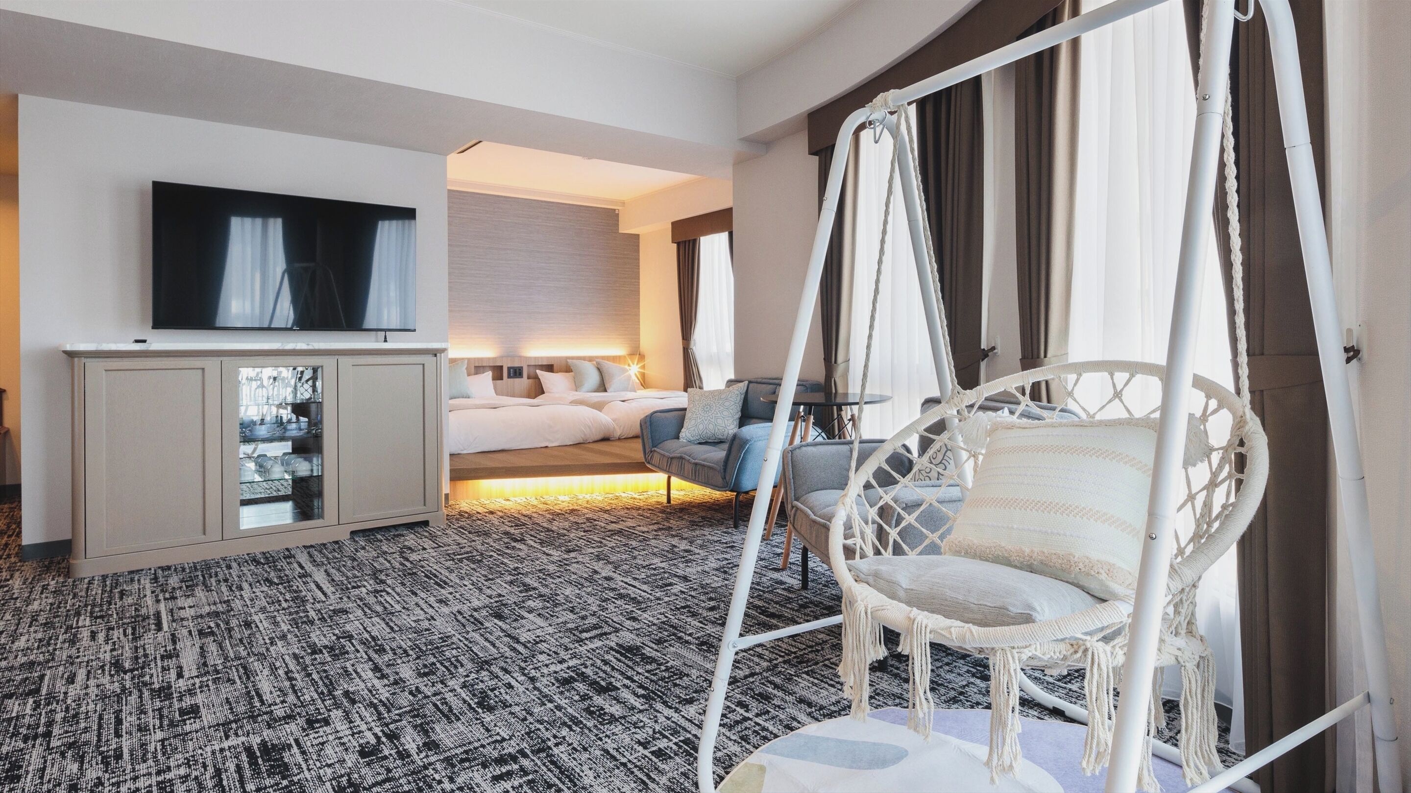 A hotel room with a bed, a TV, a seating area with chairs, and a large window.