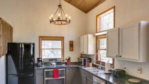 A modern kitchen with stainless steel appliances, wooden cabinets, and a chandelier.
