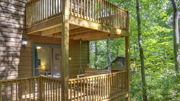 A two-story wooden deck with a glass door and a hanging swing chair.