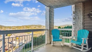 A balcony with two turquoise Adirondack chairs and a small table, overlooking a residential area with houses and a clear blue sky.