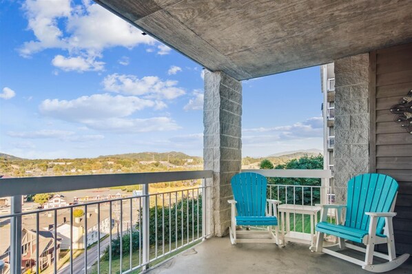 A balcony with two turquoise Adirondack chairs and a small table, overlooking a residential area with houses and a clear blue sky. - Whispering Pines 124 by Jackson Mountain Rentals (Pigeon Forge)