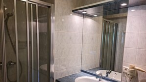 Een badkamer met een douche met glazen wand, een witte wastafel met een marmeren blad en een spiegel boven de wastafel.