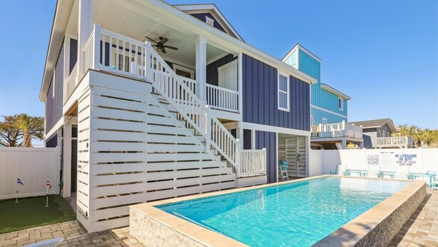 Una casa de dos pisos con piscina, un porche cubierto y una escalera que sube al nivel superior.