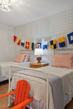 A bedroom with two beds, a chair, and a wall with patterned wallpaper.