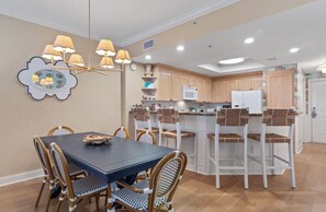 A modern kitchen with wooden cabinets, a central island, and a dining area with wicker chairs.