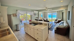 Une cuisine moderne dotée d’un îlot central, un coin repas avec vue et un espace de vie comprenant un canapé et une vue sur la mer.