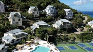 Un complexe hôtelier doté d’une grande piscine, de courts de tennis et de villas situées sur une colline.