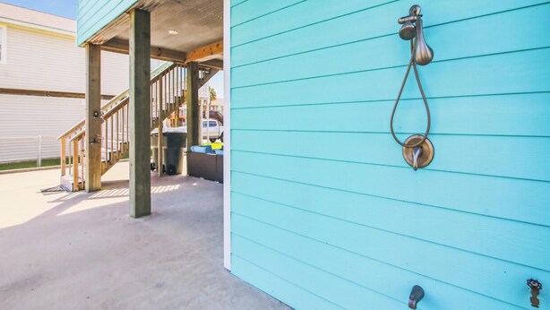 A turquoise building exterior with a metal door knocker and a staircase leading to an upper level. - The Wooden Fin by Ryson Vacation Rentals (Galveston)