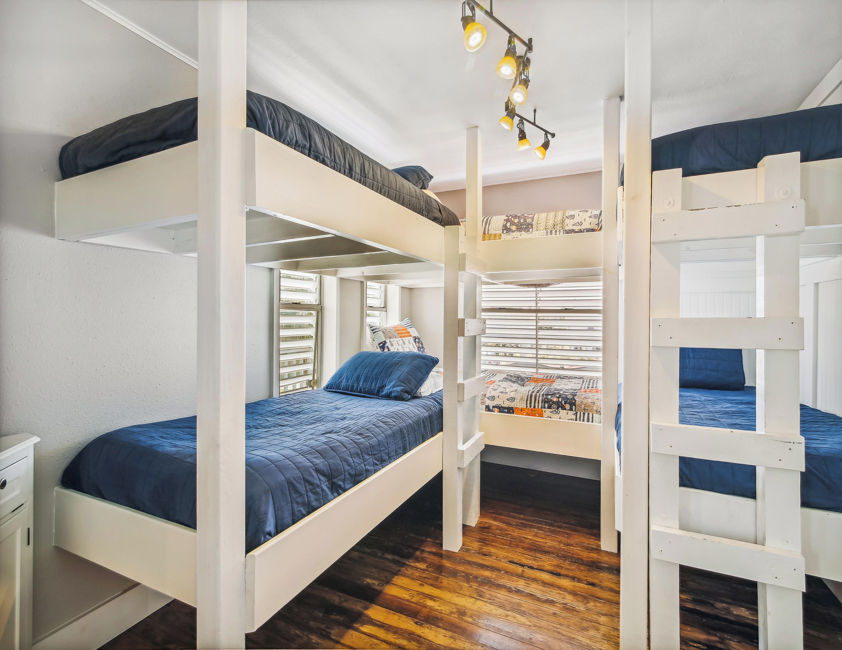 A bunk bed room with a wooden floor, white walls, and a window with blinds.