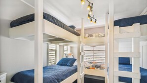 A bunk bed room with a wooden floor, white walls, and a window with blinds. - The Wooden Fin by Ryson Vacation Rentals (Galveston)