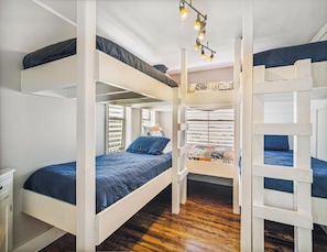 Dormitorio con literas, suelo de madera, paredes blancas y una ventana con persianas.