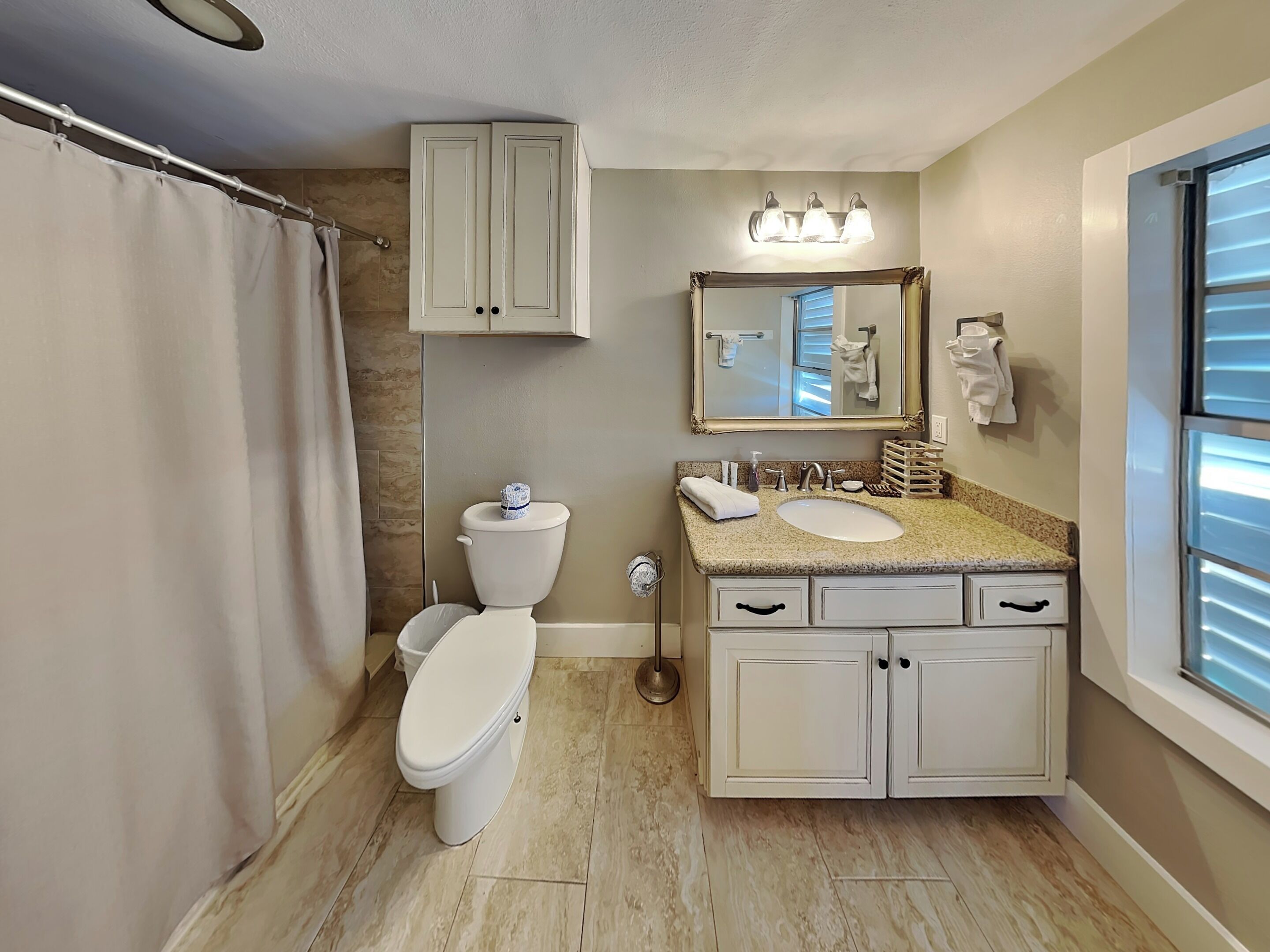 A bathroom with a toilet, sink, vanity, mirror, and shower curtain.