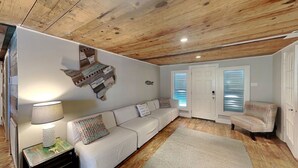 A living room with a white sofa, a patterned rug, a lamp, and a wooden ceiling. - The Wooden Fin by Ryson Vacation Rentals (Galveston)