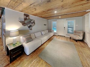 A living room with a white sofa, a patterned rug, a lamp, and a wooden ceiling.