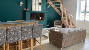 Un saló modern amb parets color turquesa, una escala de fusta, un sofà de vimet, una taula de cafè de vidre i una zona de bar amb tamborets.