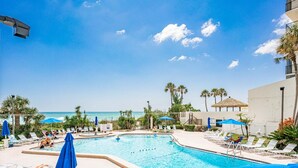 A pool area with lounge chairs and umbrellas, overlooking a beach. - Ocean Sands 1101 by Distinctive Beach Rentals (Madeira Beach)