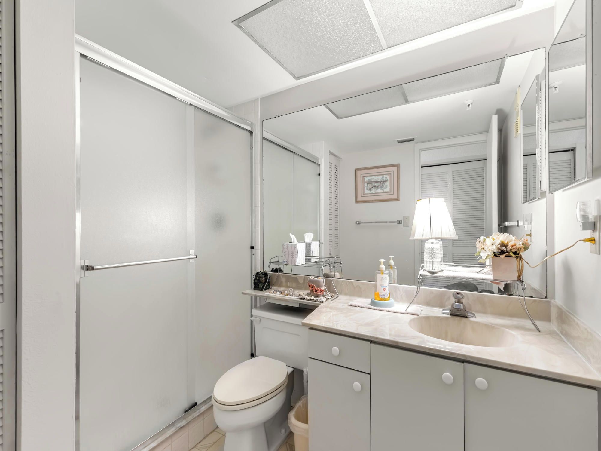 Et moderne badeværelse med toilet, vask og spejl. Der er en håndklæderække, en lille hylde med toiletartikler og et billede i ramme på væggen.