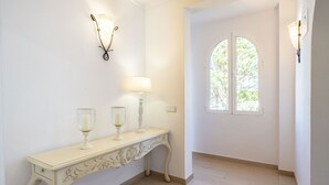 A hallway with a cream-colored console table, two wall sconces, a lamp, and a window with a view of trees. - VILLA CAS PUIG Two houses in 1 !!!!  with 2 full kitchen, air conditioned in all the rooms! (Sant Joan de Labritja / San Juan)