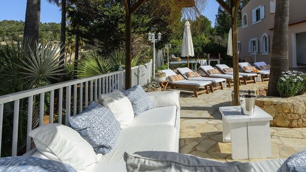 A covered outdoor seating area with white lounge chairs and a white sofa, surrounded by stone flooring and greenery. - VILLA CAS PUIG Two houses in 1 !!!!  with 2 full kitchen, air conditioned in all the rooms! (Sant Joan de Labritja / San Juan)