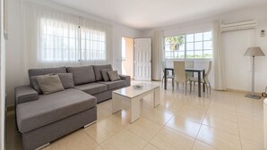 A modern living room with a grey sofa, a white coffee table, and a dining area with a table and chairs. - VILLA CAS PUIG Two houses in 1 !!!!  with 2 full kitchen, air conditioned in all the rooms! (Sant Joan de Labritja / San Juan)