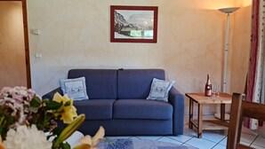 Una sala de estar con un sofá, una mesa con una botella y vasos, y un cuadro en la pared.