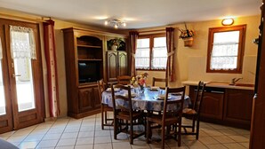Comedor con una mesa redonda, sillas, televisor y zona de cocina con armarios y fregadero.