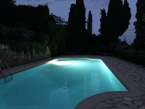 Une piscine rectangulaire bordée de pierres, entourée d’un chemin de pierre et d’un mur de pierre agrémenté de verdure.