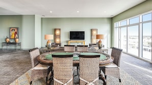 A conference room with a round table, wicker chairs, and a large window with a city view. - Emerald 705 by Ryson Vacation Rentals (Galveston)
