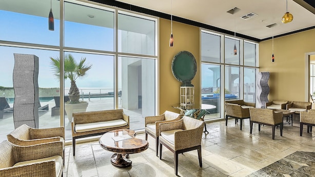 A spacious indoor area with large windows, wicker furniture, and a view of the outdoors. - Emerald 705 by Ryson Vacation Rentals (Galveston)