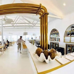 A modern interior with a curved golden structure, a bar area with shelves of bottles, and a seating area with tables and chairs. - Manly Oasis, 5bd, 3 King bd,Pool (Manly)