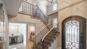 Un vestíbulo espacioso con una imponente escalera, un espejo grande y una puerta decorativa.