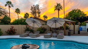 Zona de piscina con sillones de descanso, sombrillas y un jacuzzi.