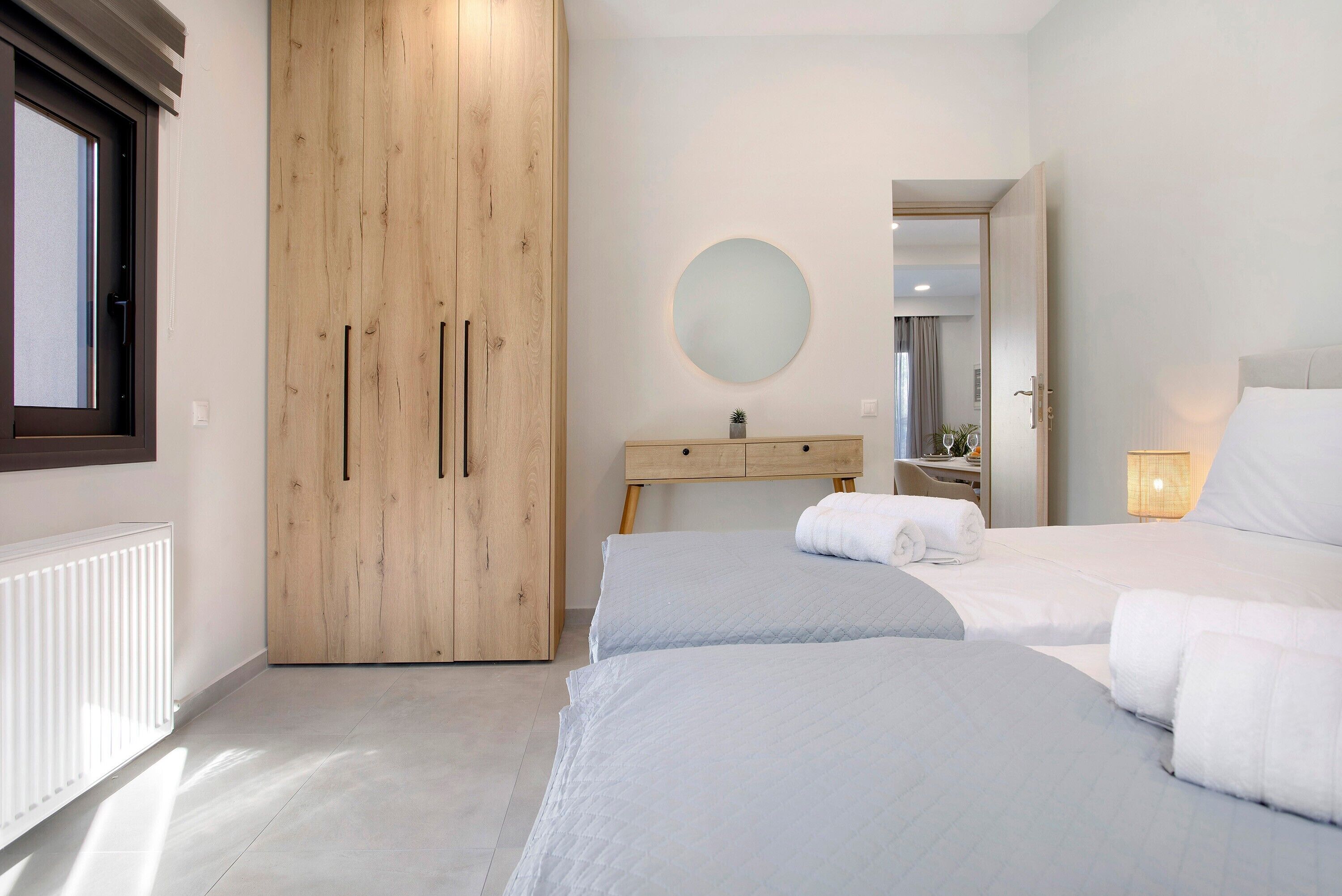 A bedroom with two beds, a wooden wardrobe, a round mirror, and a bedside table.