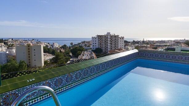 En swimmingpool med utsikt över havet och byggnader i bakgrunden.