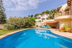 A swimming pool with lounge chairs, surrounded by greenery and a building with a balcony. - "Villa Rafael" with Sea View, Pool & Wi-Fi (El Poble Nou de Benitatxell)