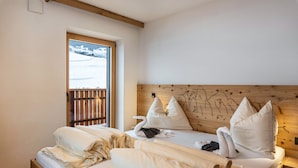 A hotel room with a wooden headboard, a bed with neatly folded white linens, a window with a view of a snowy landscape, and a wooden floor. - Farm 'Enzian' with Mountain View, Shared Terrace and Wi-Fi (Funes)