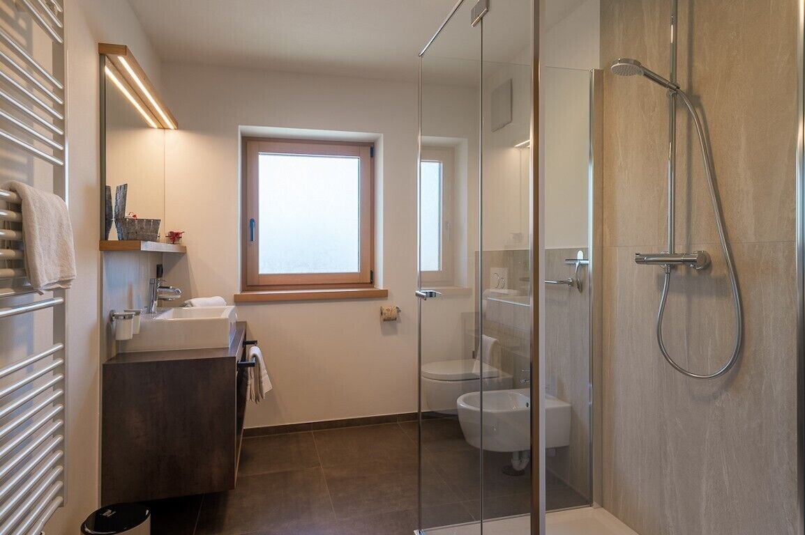 Ein modernes Badezimmer mit Duschkabine aus Glas, Toilette, Waschbecken mit Spiegel und Fenster.