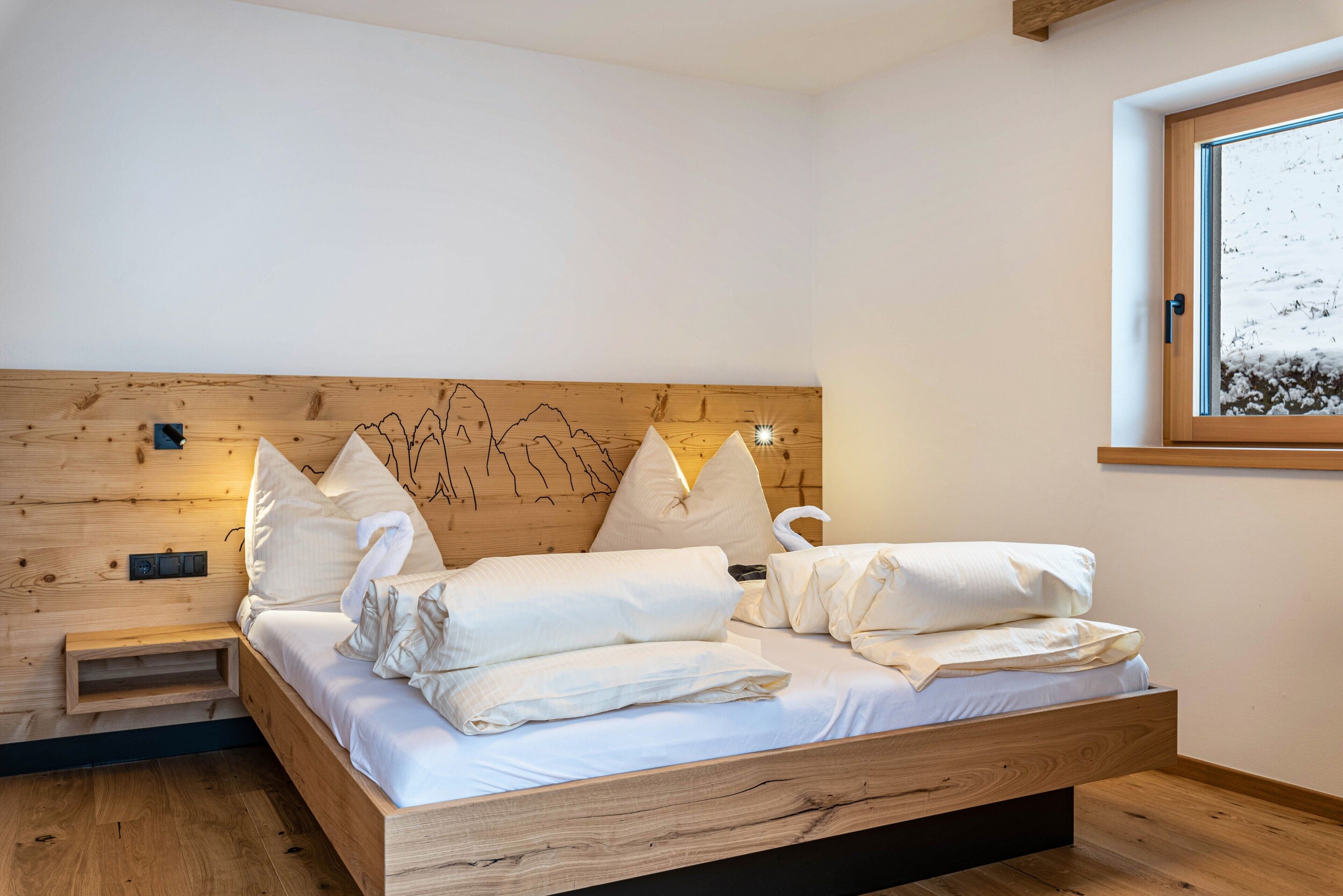Un letto di legno con biancheria bianca, un comodino e una lampada fissata al muro.