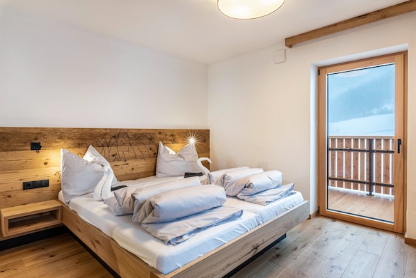 Una cama doble con cabecera de madera, una mesita de noche y un amplio ventanal corredero a un balcón.