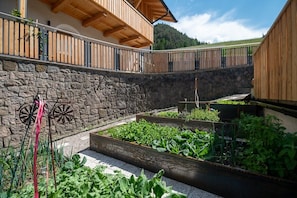 Un muro de piedra con barandas de madera, un balcón de madera y macetas elevadas con diversas plantas.