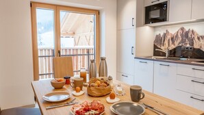 A breakfast table with food, drinks, and utensils in a modern kitchen with a mountain view. - Holiday Apartment "Planerhof Apartment Lilie" with Mountain View, Shared Terrace and Wi-Fi (Funes)