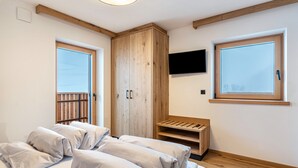 A bedroom with a bed, a wooden wardrobe, a TV mounted on the wall, and a window. - Holiday Apartment "Planerhof Apartment Lilie" with Mountain View, Shared Terrace and Wi-Fi (Funes)